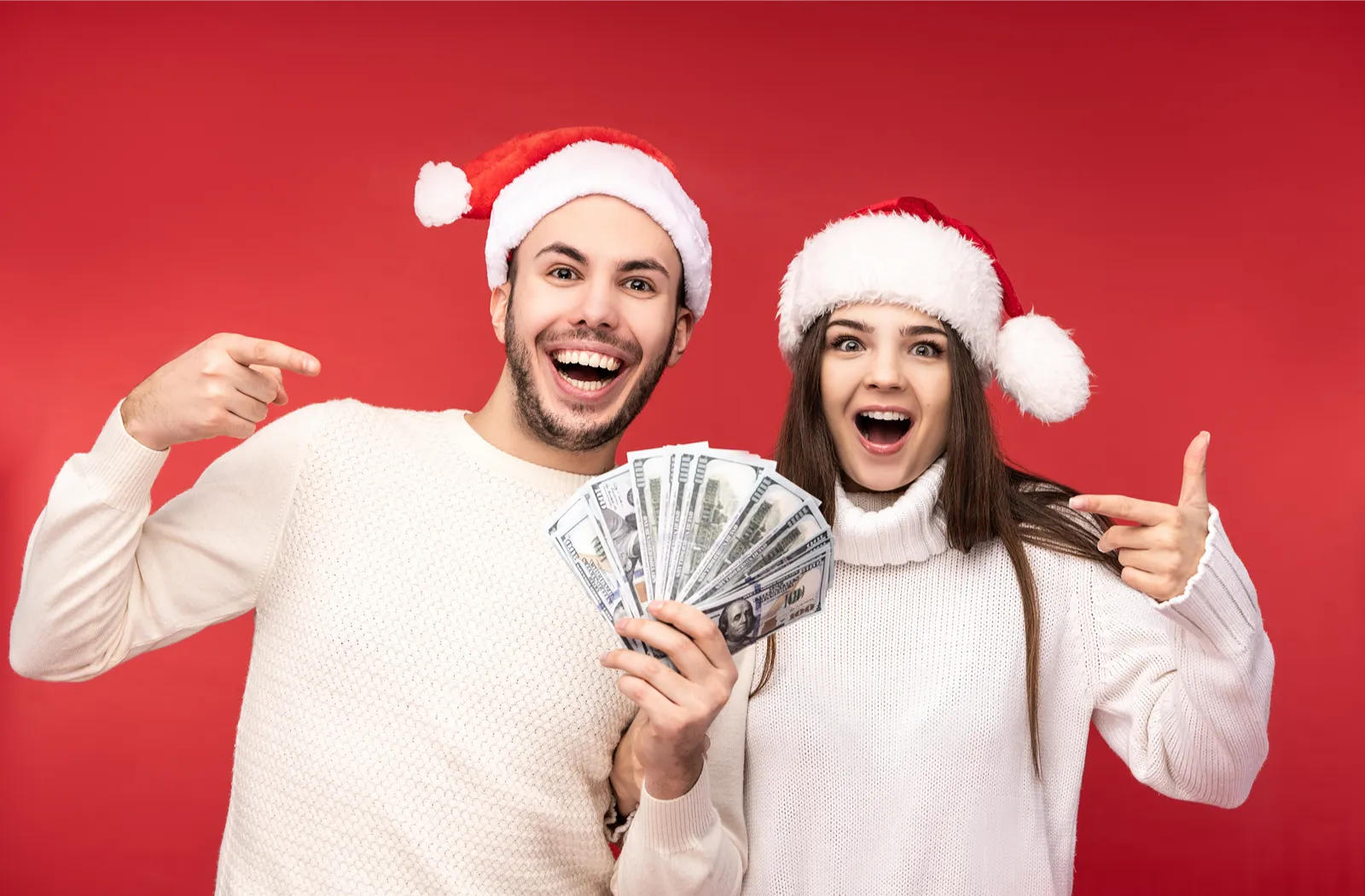 photo sweet couple christmas hats happy about holidays holds money dollars male female are love look blessed smile isolated red background